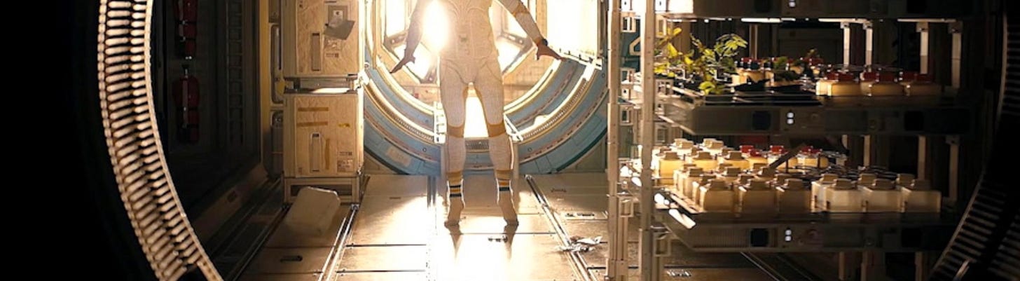 Ryan Gosling as Ryland Grace in a spacesuit, backlit at the end of a spacecraft corridor lined with lab equipment and plants