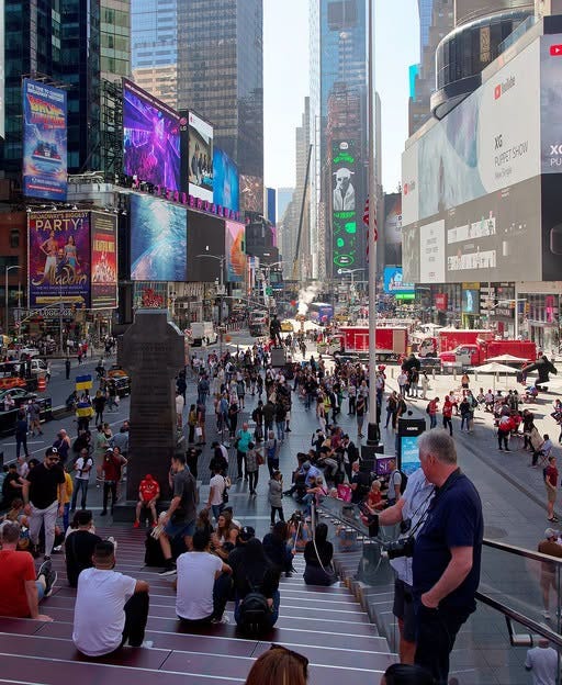 May be an image of crowd, skyscraper, Times Square and text