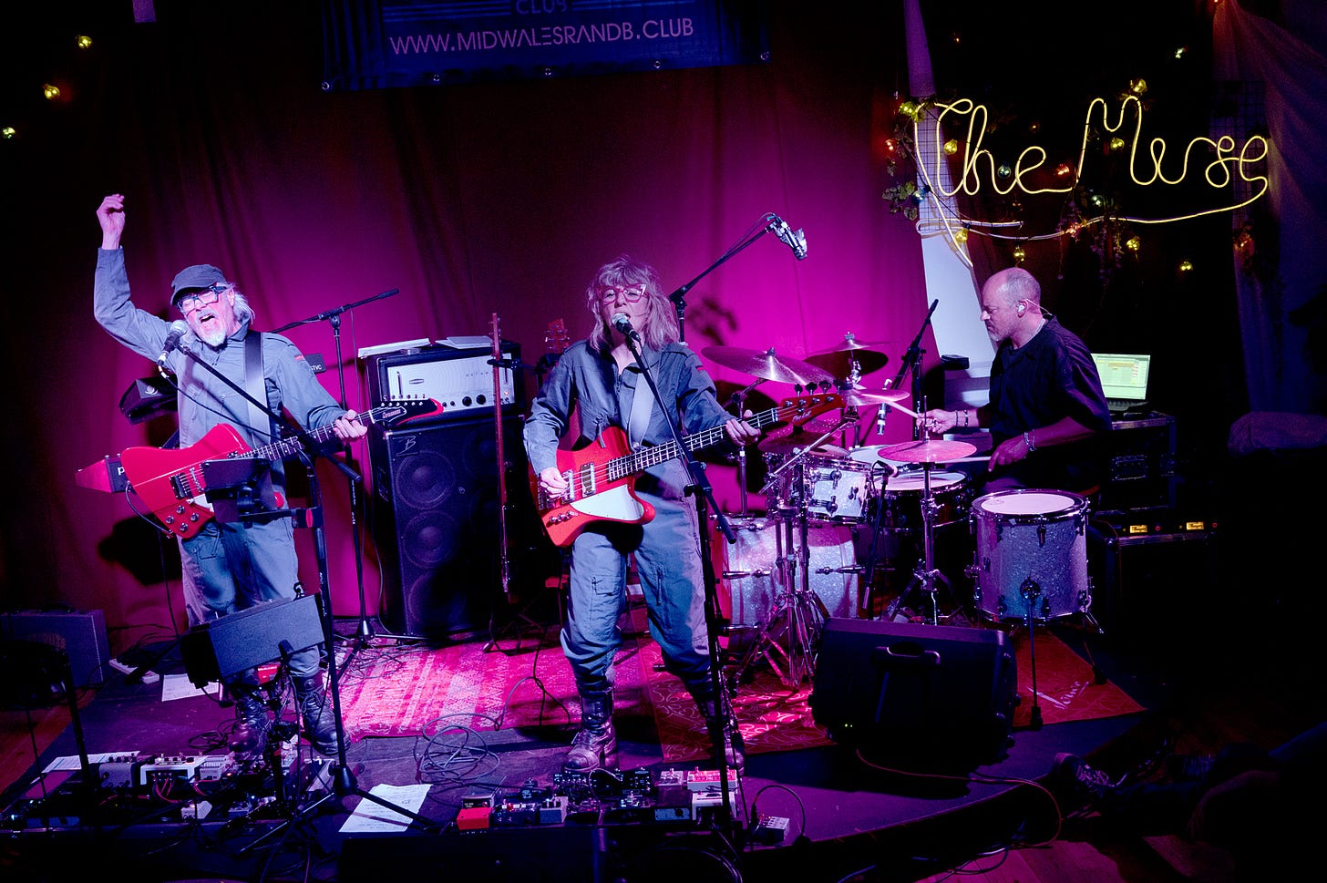 A man singing and playing guitar, a woman singing and playing bass guitar in the middle - a man playing drums on the right - Starlite & Campbell concert - The Muse, Brecon. Wales