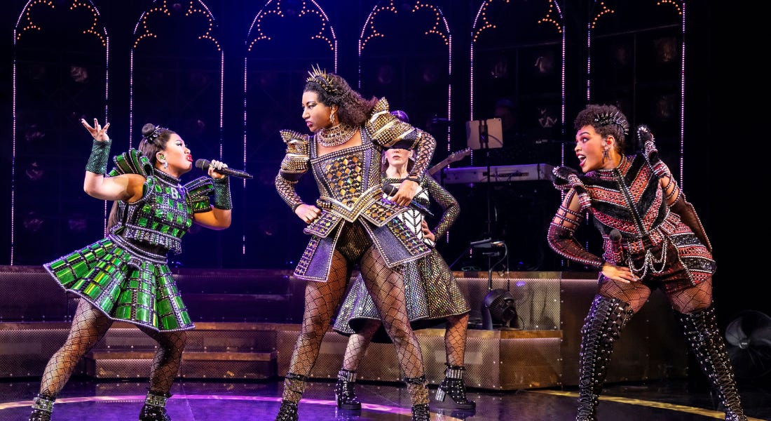 A group of women on stage wearing jewelled dresses and fishnets singing into microphones