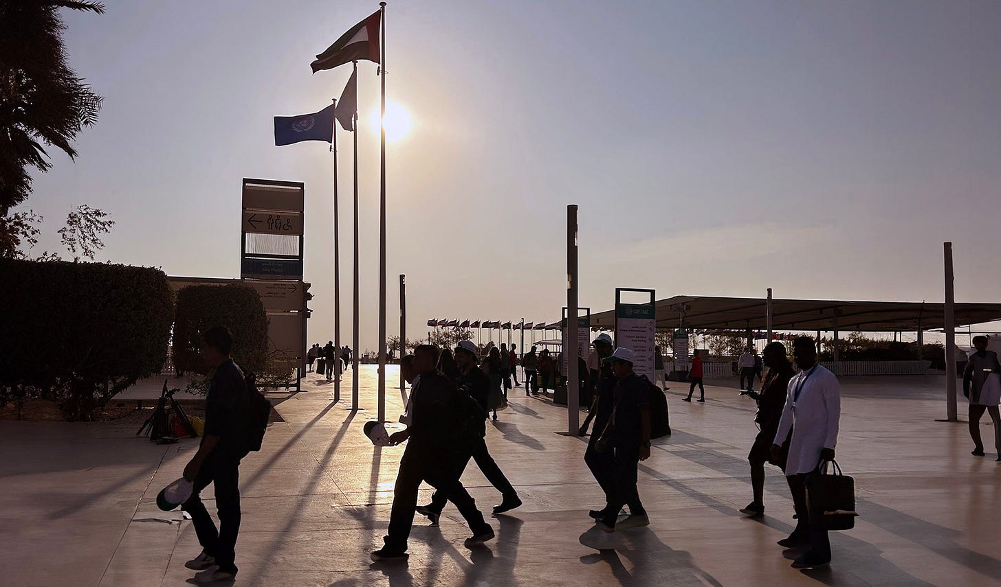 People walking past UAE and UN flags as the sun sets