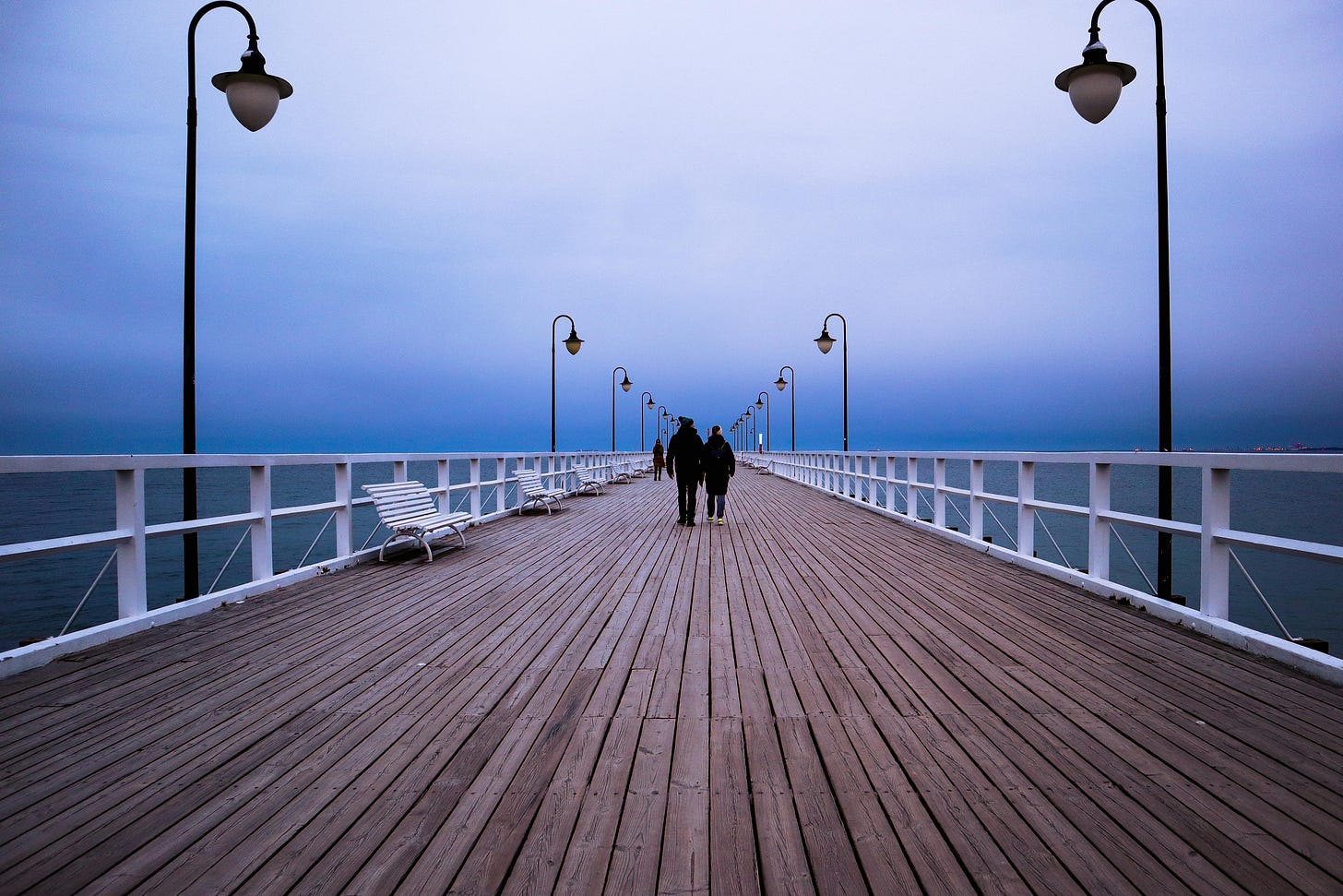 People walking on pier floating between water and horizon