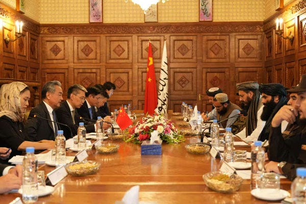 Chinese Foreign Minister Wang Yi (left) meets with a delegation of the Taliban-led government in Afghanistan led by Taliban Interior Minister Sirajuddin Haqqani (right). The group is seated at a long table with the flags of the People's Republic of China and Islamic Emirate of Afghanistan in the background. Chinese Foreign Minister Wang Yi (left) meets with a delegation of the Taliban-led government in Afghanistan led by Taliban Interior Minister Sirajuddin Haqqani (right). The group is seated at a long table with the flags of the People's Republic of China and Islamic Emirate of Afghanistan in the background.