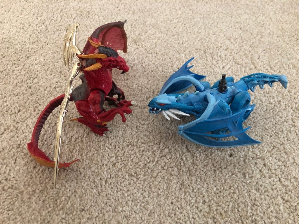 A blue and a red toy dragon facing each other on a beige background. The red dragon has golden wings A blue and a red toy dragon facing each other on a beige background. The red dragon has golden wings