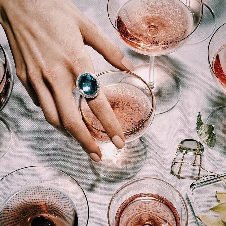This may contain: a woman's hand with a ring on top of several glasses filled with wine