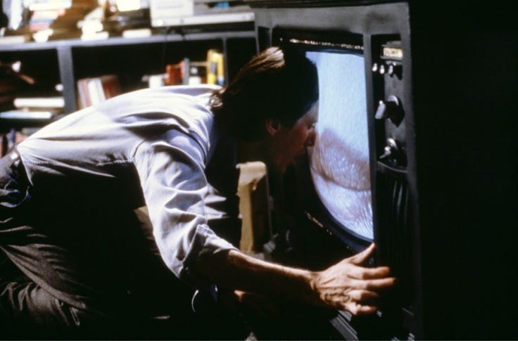 This may contain: a man leaning over to look at a television screen with his hand on the monitor