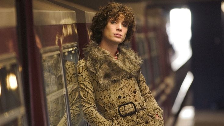This may contain: a woman standing on a subway platform wearing a fur coat and holding her hands in her pockets