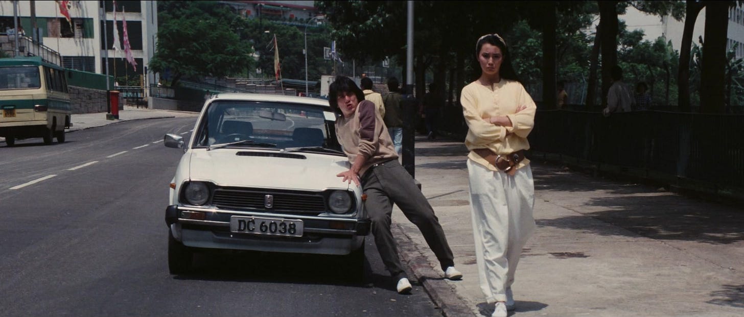 A man is trying to keep a small white car from rolling forward while a woman stands with her arms crossed looking annoyed. A man is trying to keep a small white car from rolling forward while a woman stands with her arms crossed looking annoyed.