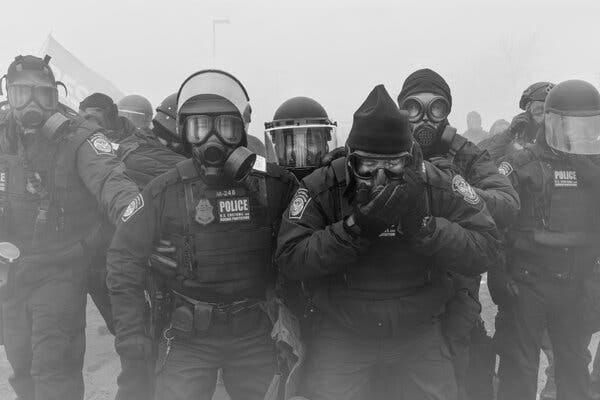 A line of armed federal law enforcement agents in gas masks and riot helmets. A line of armed federal law enforcement agents in gas masks and riot helmets.