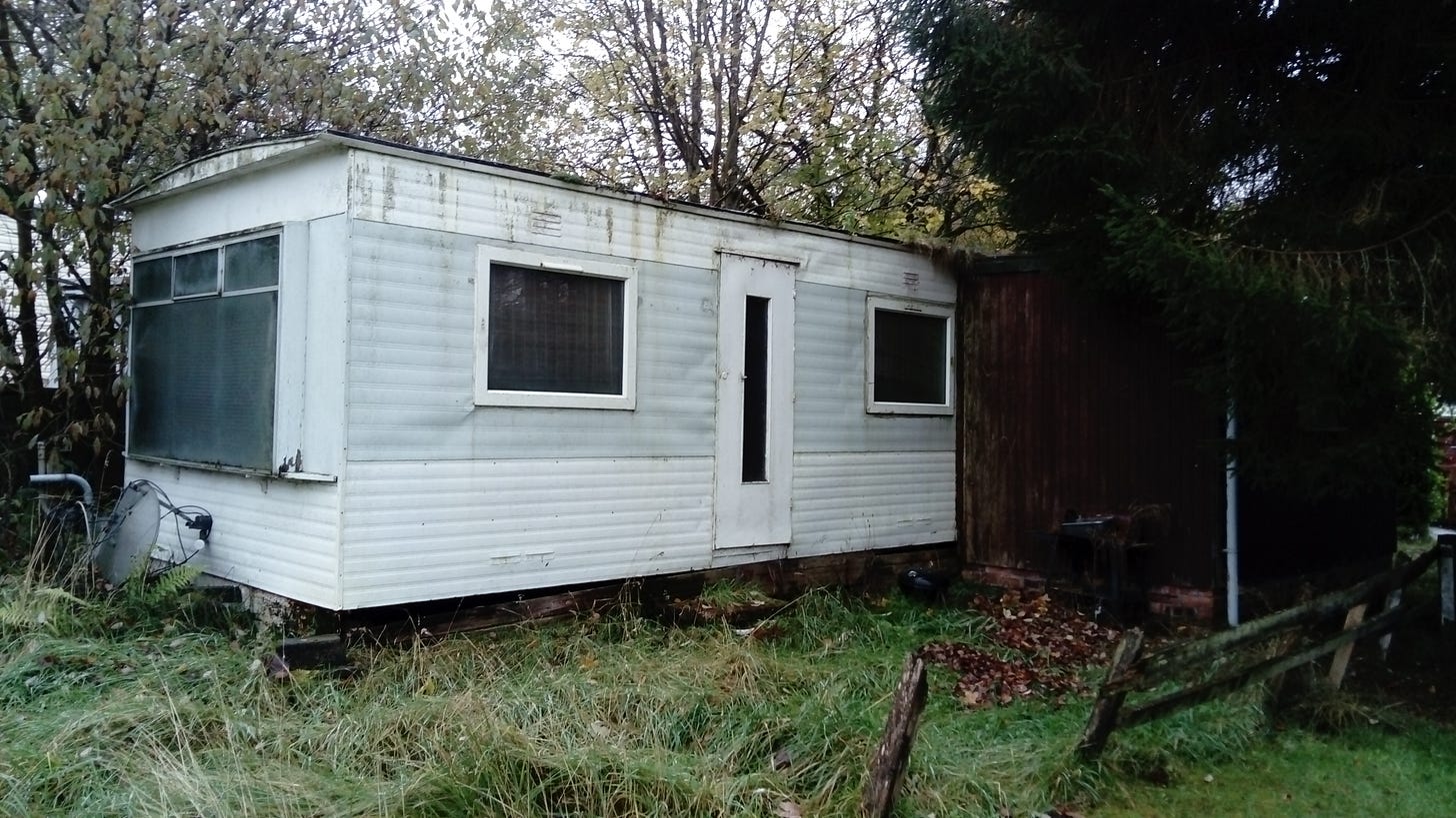 A dilapidated trailer-style home surrounded by overgrown grass.
