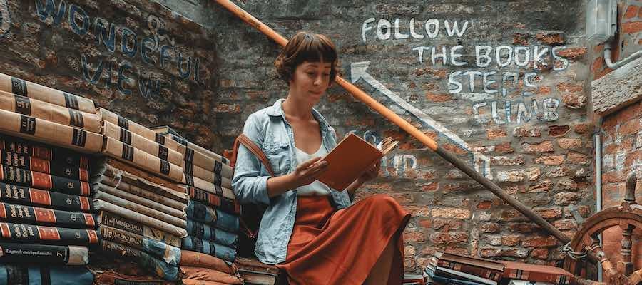 Lady reading a book while sitting on a stack of books