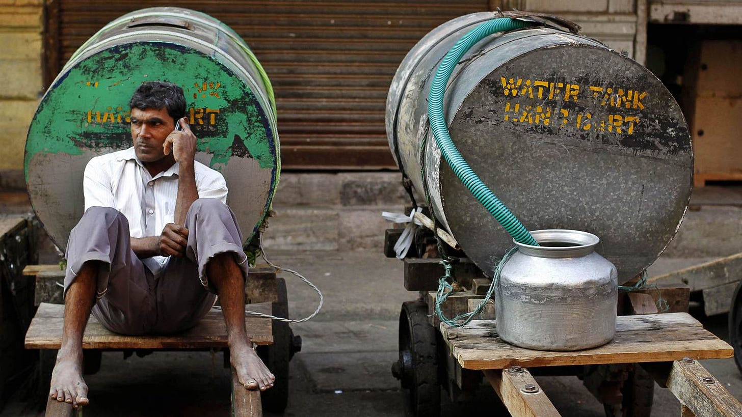 A man sitting in the backdrop of a water facility in a village, listening to mobile Vaani on his phone