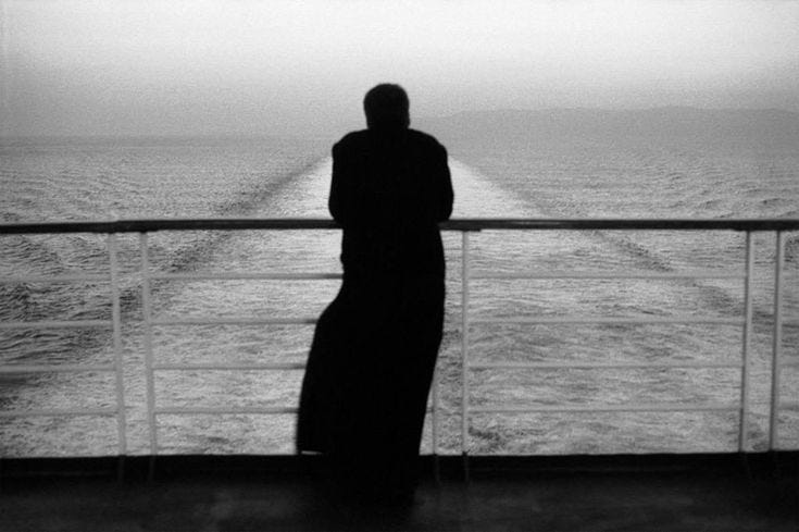 This may contain: a person standing on a boat looking out at the ocean in black and white photo This may contain: a person standing on a boat looking out at the ocean in black and white photo