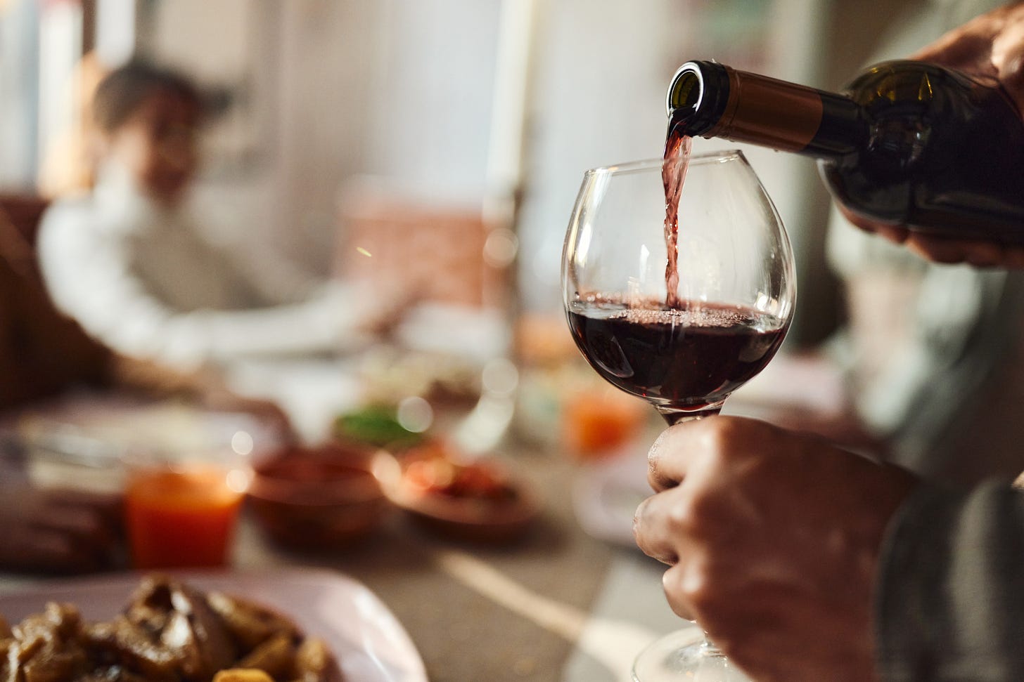 Pouring red wine into a glass at a social gathering