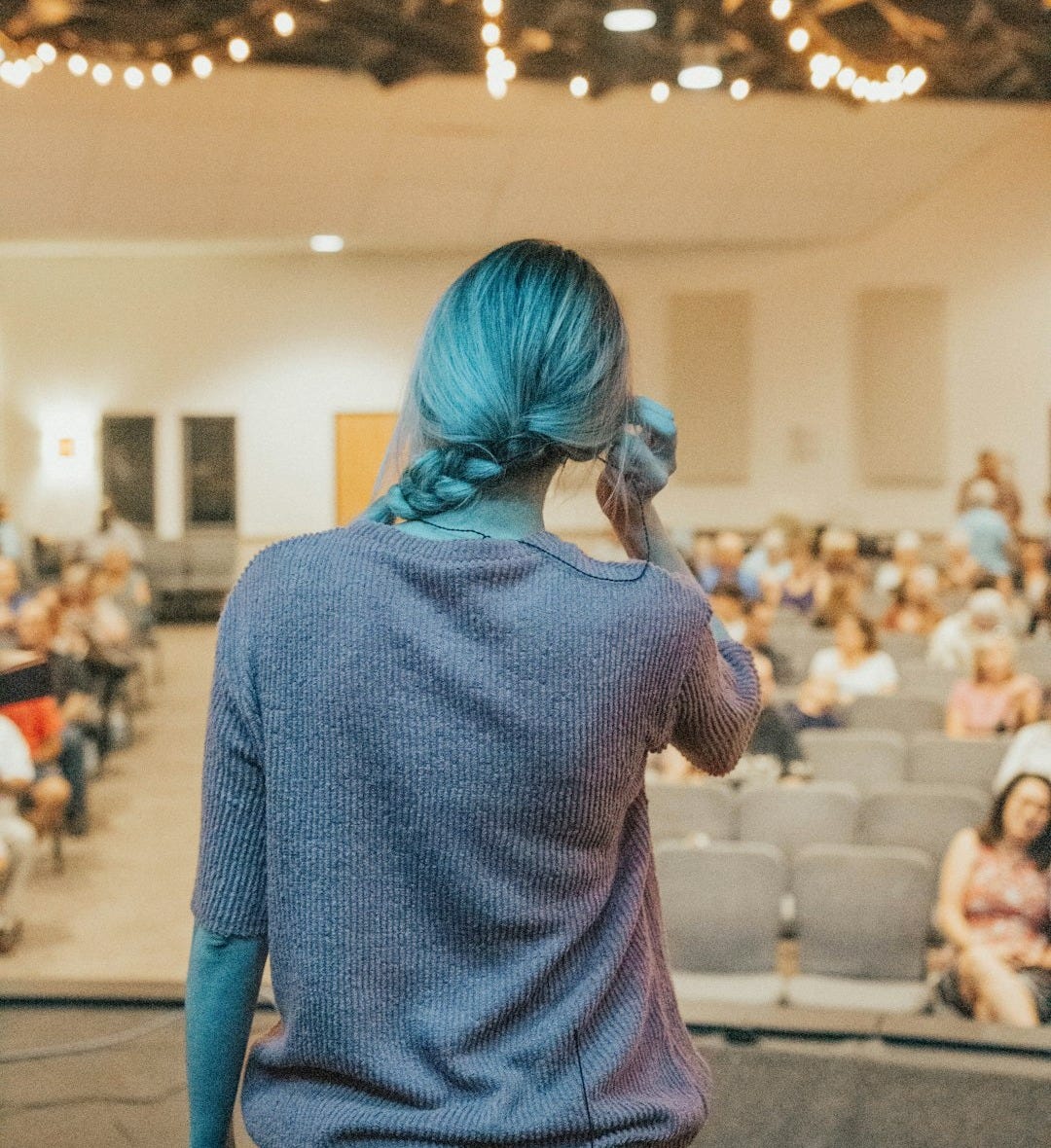 a woman with blue hair standing in front of an audience a woman with blue hair standing in front of an audience