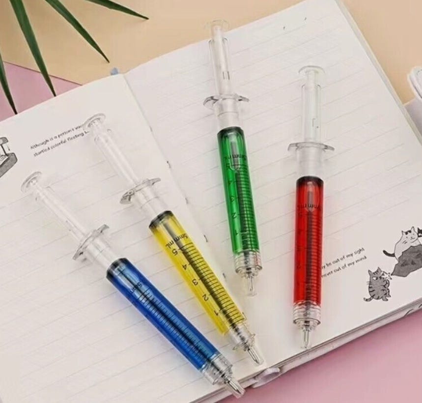 Four pens that look like hypodermic needles, filled with red, yellow, blue, and green ink laying on a journal. Four pens that look like hypodermic needles, filled with red, yellow, blue, and green ink laying on a journal.
