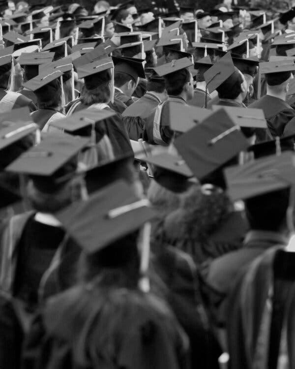 A large group of students in black caps and gowns at a commencement ceremony.