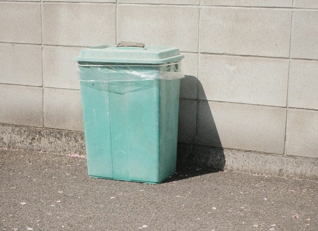 green plastic trash bin beside white wall