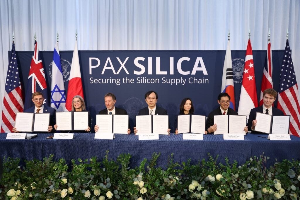 Representatives from multiple countries sit at a table holding signed documents in front of a backdrop that reads "PAX SILICA: Securing the Silicon Supply Chain," with national flags displayed behind them.