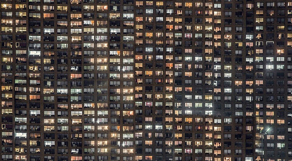Rows of illuminated apartment windows at night, each revealing only a fragment of the life inside. Rows of illuminated apartment windows at night, each revealing only a fragment of the life inside.