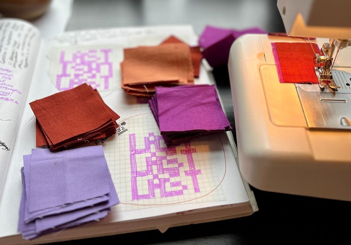 the word “LAST” drawn out on grid paper in a sketchbook, which lays to the left of a sewing machine. Atop the sketchbook are stacks of squares of 4 different solid fabrics waiting to be stitched together following the pattern on the grid paper. the word “LAST” drawn out on grid paper in a sketchbook, which lays to the left of a sewing machine. Atop the sketchbook are stacks of squares of 4 different solid fabrics waiting to be stitched together following the pattern on the grid paper.