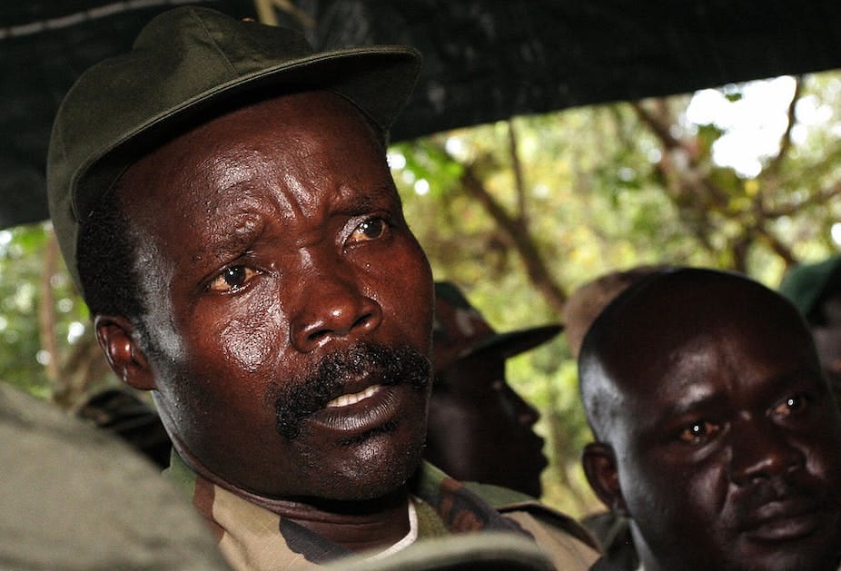 A close-up shot of a man in a brown and green military uniform and green hat speaking. There are other men in the background dressed similarly. A close-up shot of a man in a brown and green military uniform and green hat speaking. There are other men in the background dressed similarly.
