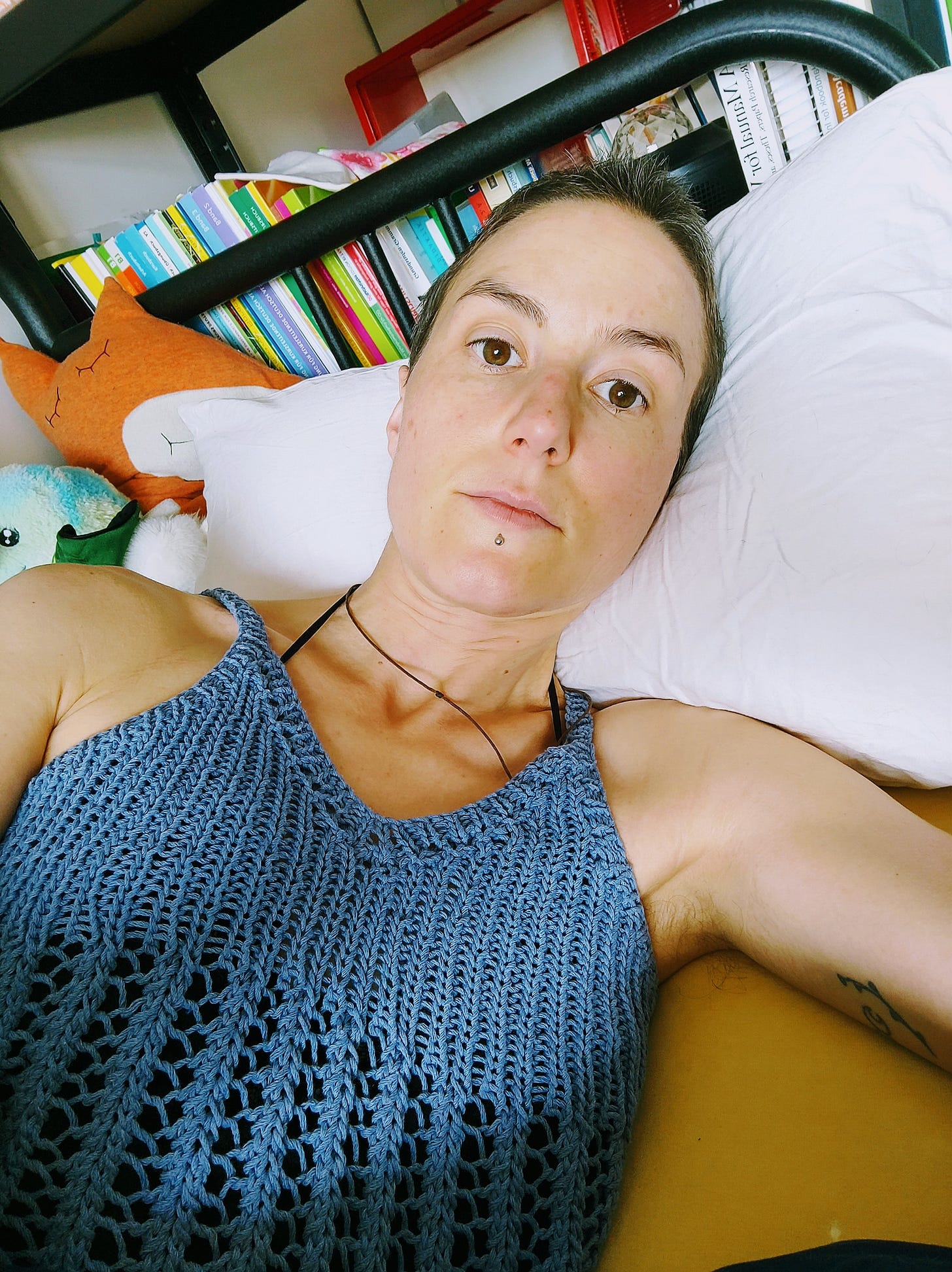 The photo shows the author Yvonne, a white woman with short brown hair lying on her bed. She is wearing a blue knitted top to help raise awareness for ME/CFS.