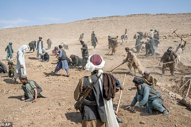 A Taliban fighter, foreground, watches over laborers building a road in a remote region of Afghanistan