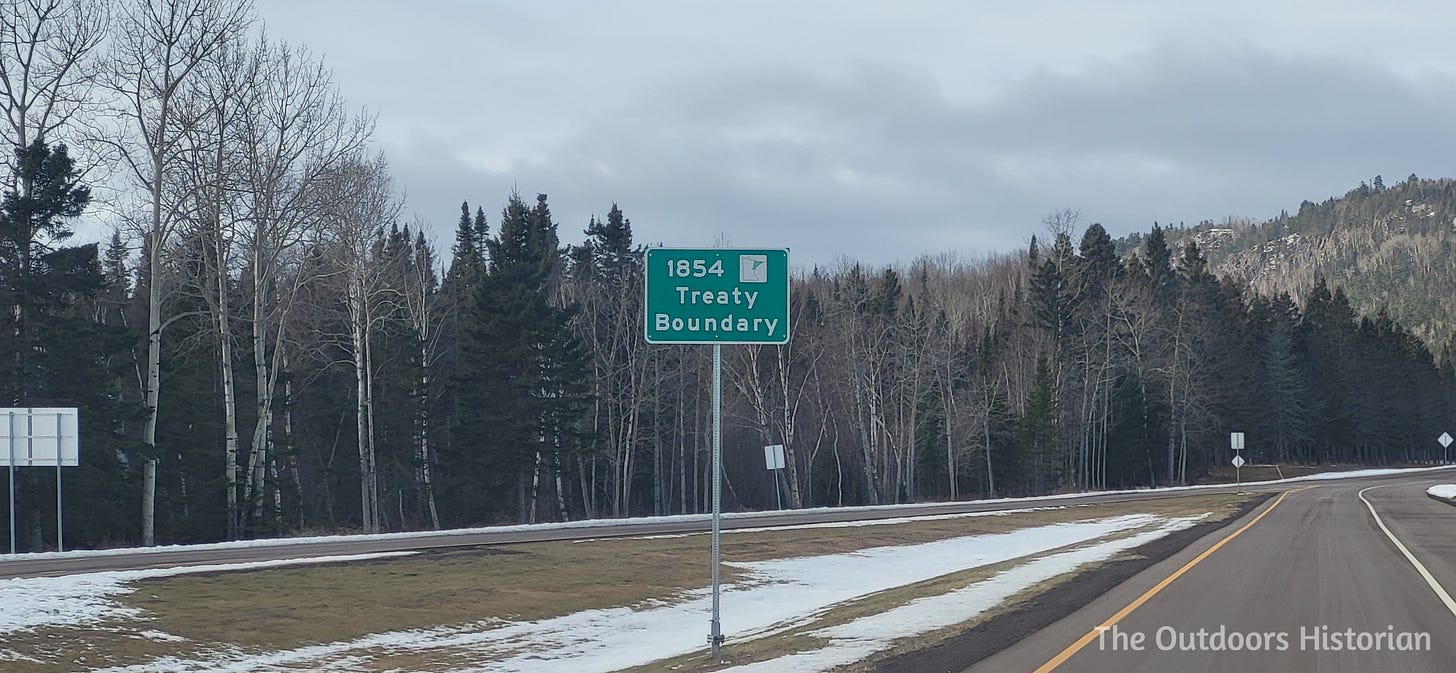 A sign saying "1854 Treaty Boundary" beside a paved, divided highway winding through forested hills.