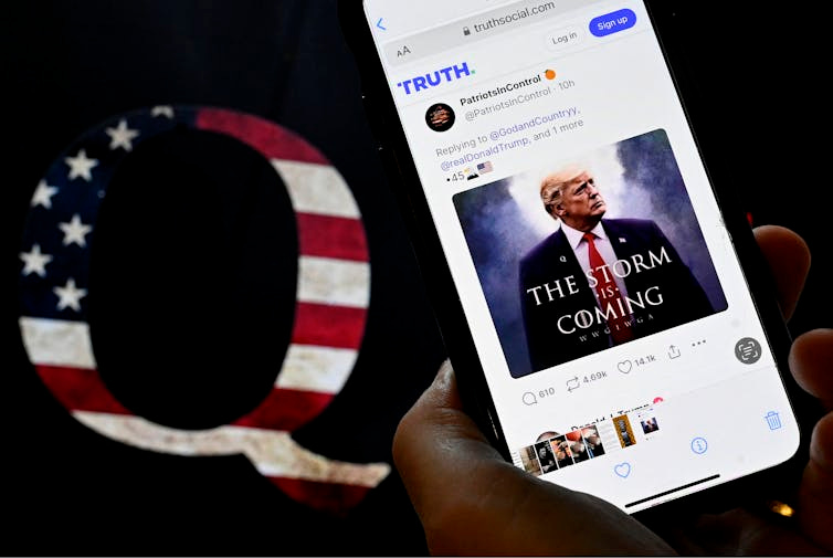 A mobile device with an image of Donald Trump alongside a QAnon sticker using an American flag. A mobile device with an image of Donald Trump alongside a QAnon sticker using an American flag.