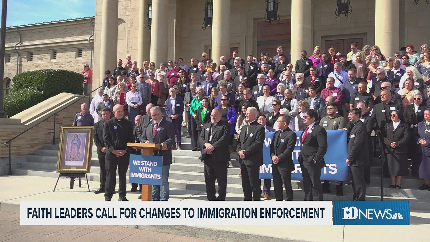 Clergy and faith leaders stand on the steps of the Knoxville cathedral behind a podium sign reading We Stand With Immigrants Clergy and faith leaders stand on the steps of the Knoxville cathedral behind a podium sign reading We Stand With Immigrants