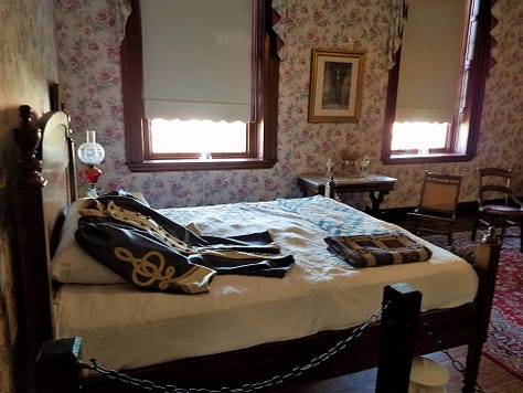 The Dickson Williams Mansion, a brick building with a white porch; the parlor, showing a round table surrounded by black chairs on a red oriental rug in front of a fireplace; the kitchen area, showing original north carolina furniture; bedrooms of the house, along with a portrait of General John Hunt Morgan sitting in a chair in a black coat with tall black boots; and the bed where he spent his last night.