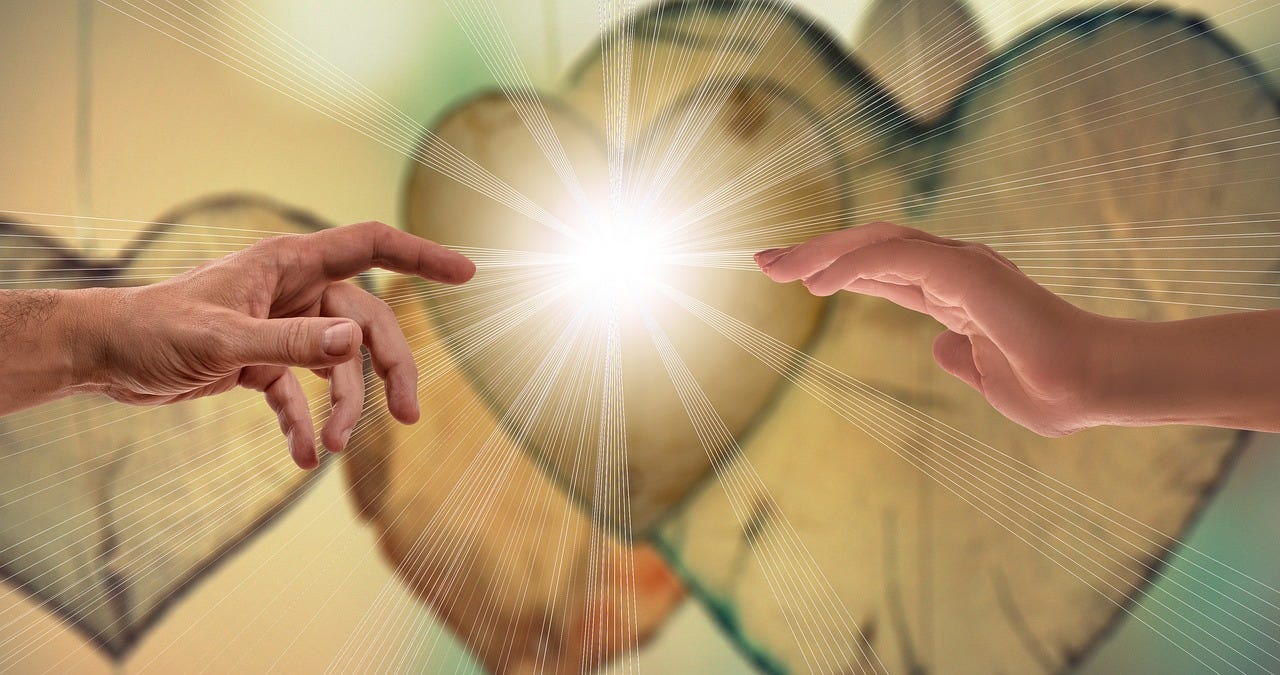 Two hands approach a radiant light with hearts in the background Two hands approach a radiant light with hearts in the background