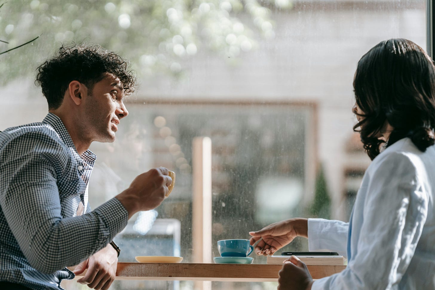 People sitting at a table by a window drinking coffee.