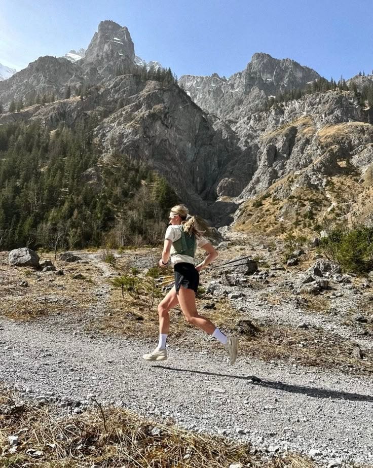 This may contain: a woman running on a trail in the mountains
