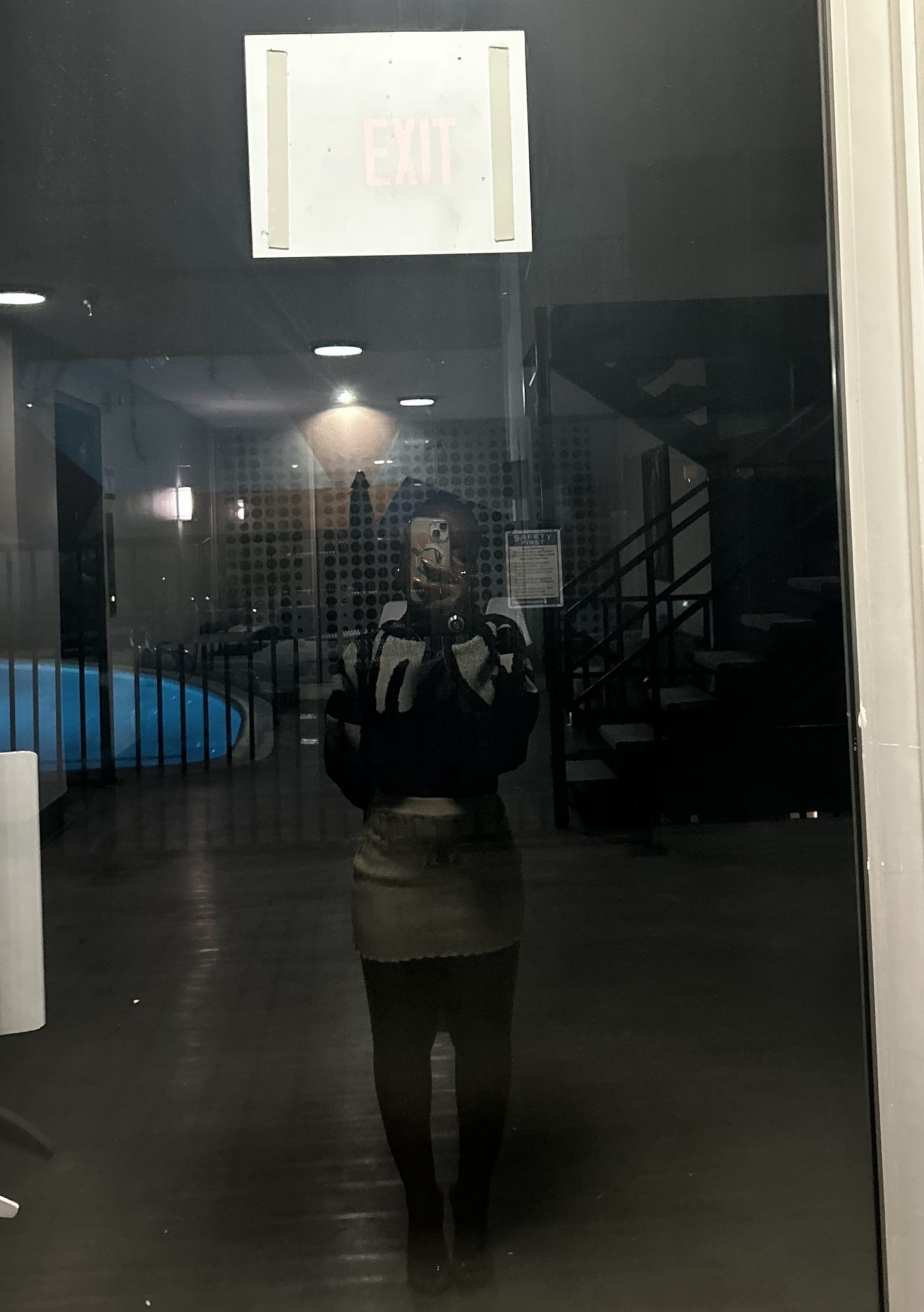 Low-light mirror self-portrait captured in a glass doorway, the subject standing beneath an illuminated exit sign. The reflection creates a moody, cinematic composition with dark architectural lines, soft indoor lighting, and a quiet, introspective atmosphere Low-light mirror self-portrait captured in a glass doorway, the subject standing beneath an illuminated exit sign. The reflection creates a moody, cinematic composition with dark architectural lines, soft indoor lighting, and a quiet, introspective atmosphere