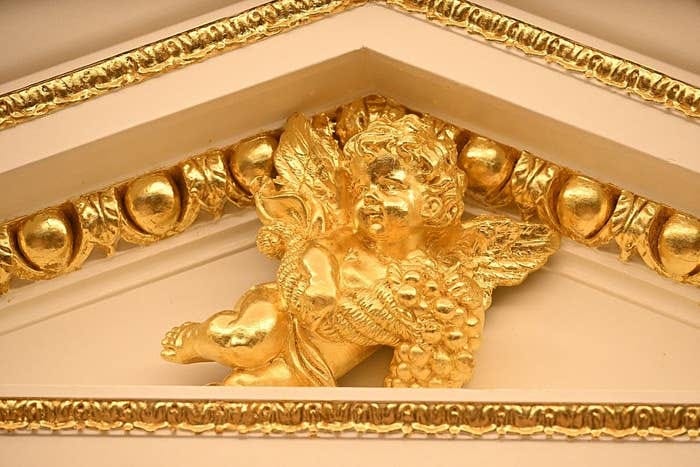 A golden cherub sculpture with intricate detailing adorns the top of an ornate architectural structure