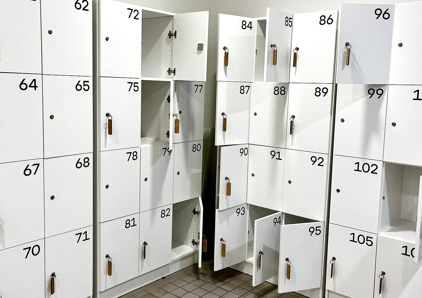 corner of a locker room - white doors marked with black numbers, some doors have keys with long wooden tags dangling