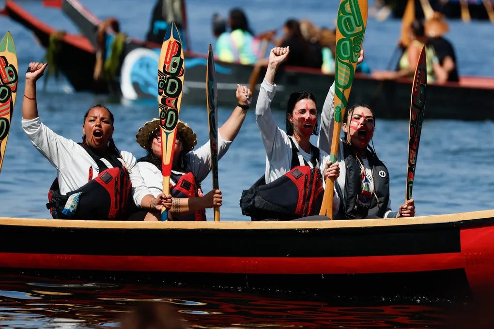 From left, Patricia Chookenshaa Allen, Noelani Kanuha Auguston, Sarah Boyles-Muehleck and Skaydu.û Jules raise their fists and yell as they paddle by Alki Beach before coming ashore during the final leg of the 2023 Canoe Journey.  (Jennifer Buchanan / The Seattle Times)