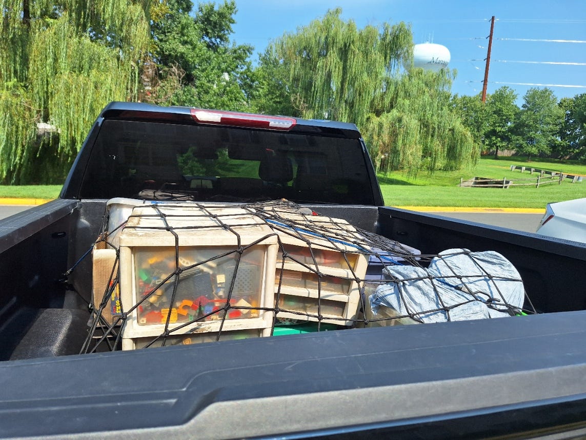 The bed of a black pickup truck holds a single layer of packed belongings secured beneath a cargo net, with empty space remaining around them. The bed of a black pickup truck holds a single layer of packed belongings secured beneath a cargo net, with empty space remaining around them.