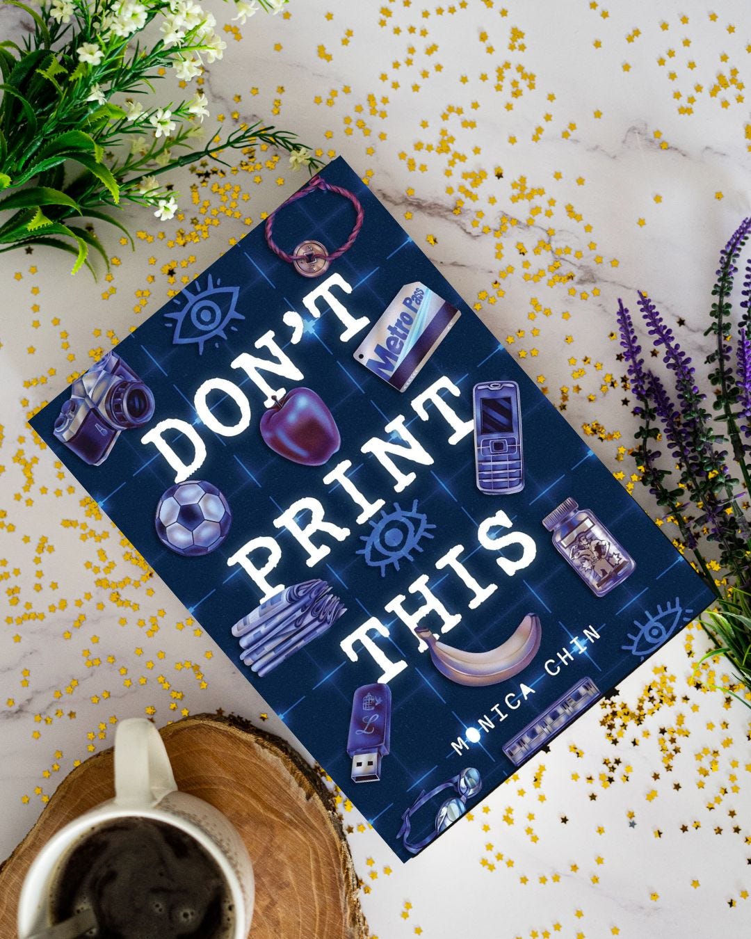 Book "Don't Print This" by Monica Chin on a table next to flowers and a drink