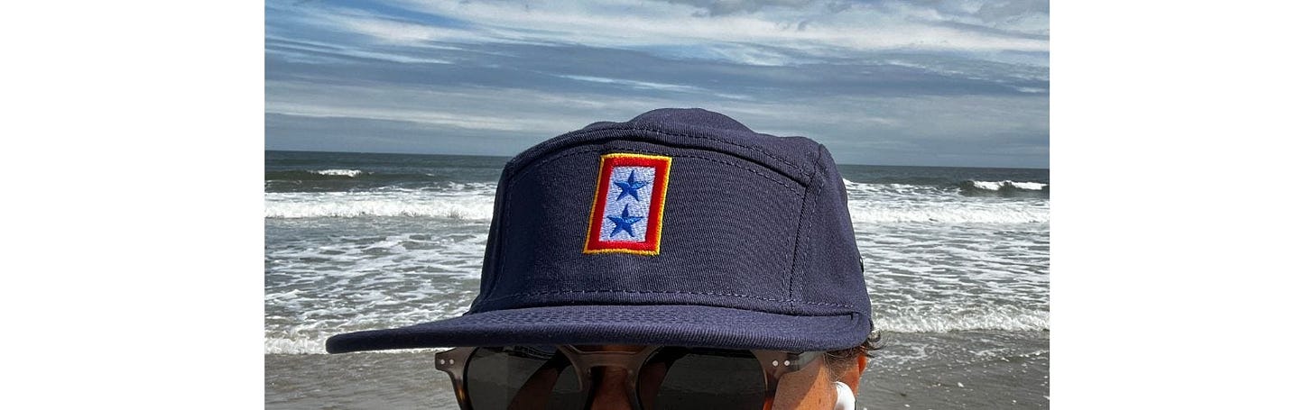 Navy cap with a badge on front of two blue stars on a white background with a red border