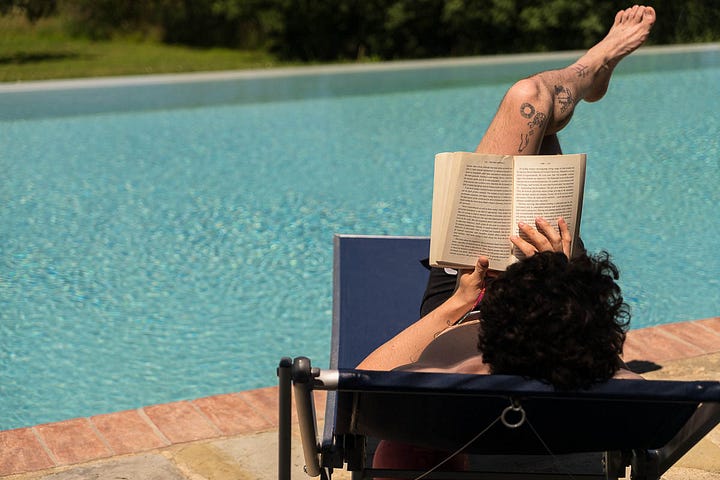 Four photos depicting candles at night, olive oil pouring from a spout, someone reading a book by the pool, and a field of flowers