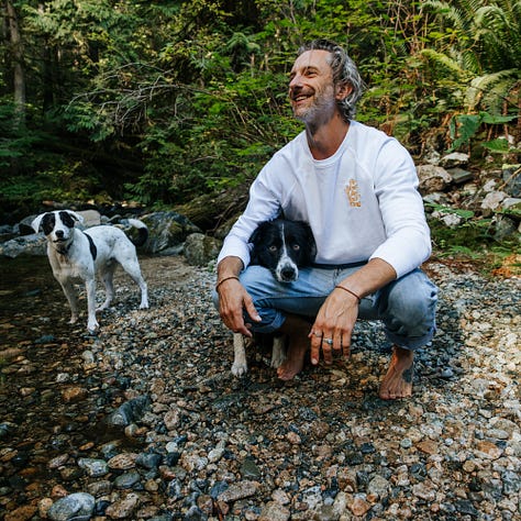 awkward man frolics around stream with dogs wearing very nice merch from be more like your dog