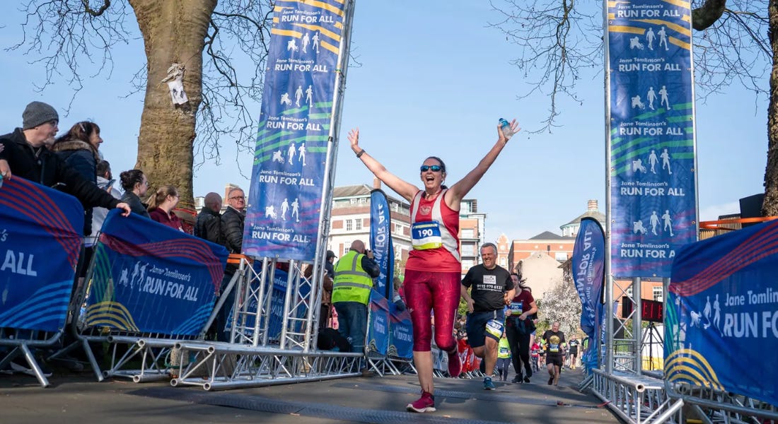 A woman in a red running outfit running across a finish line with crowds of people to the left and right of her
