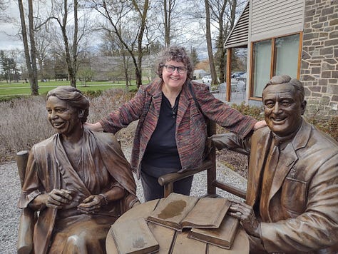 Annette with a lifesize mural of President Gerald Ford; Pulling a small covered cart on two wheels; with two kids in a museum atrium; With staues of Franklin and Eleanor Roosevelt sitting at tables; taking picture of photo exhibit; Outdoors with monuments and road in background.