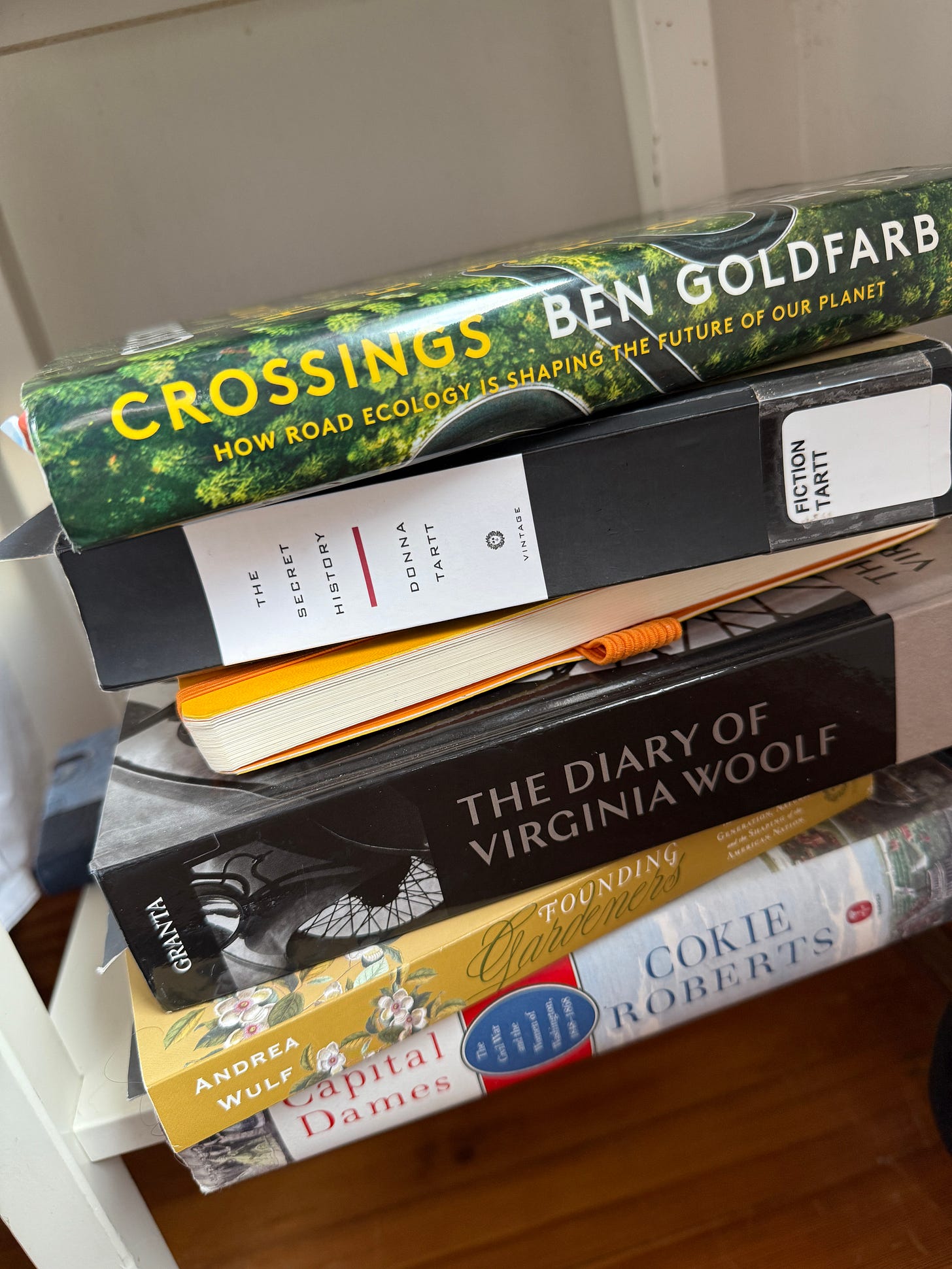 A collection of fiction and nonfiction books stacked on a nightstand shelf
