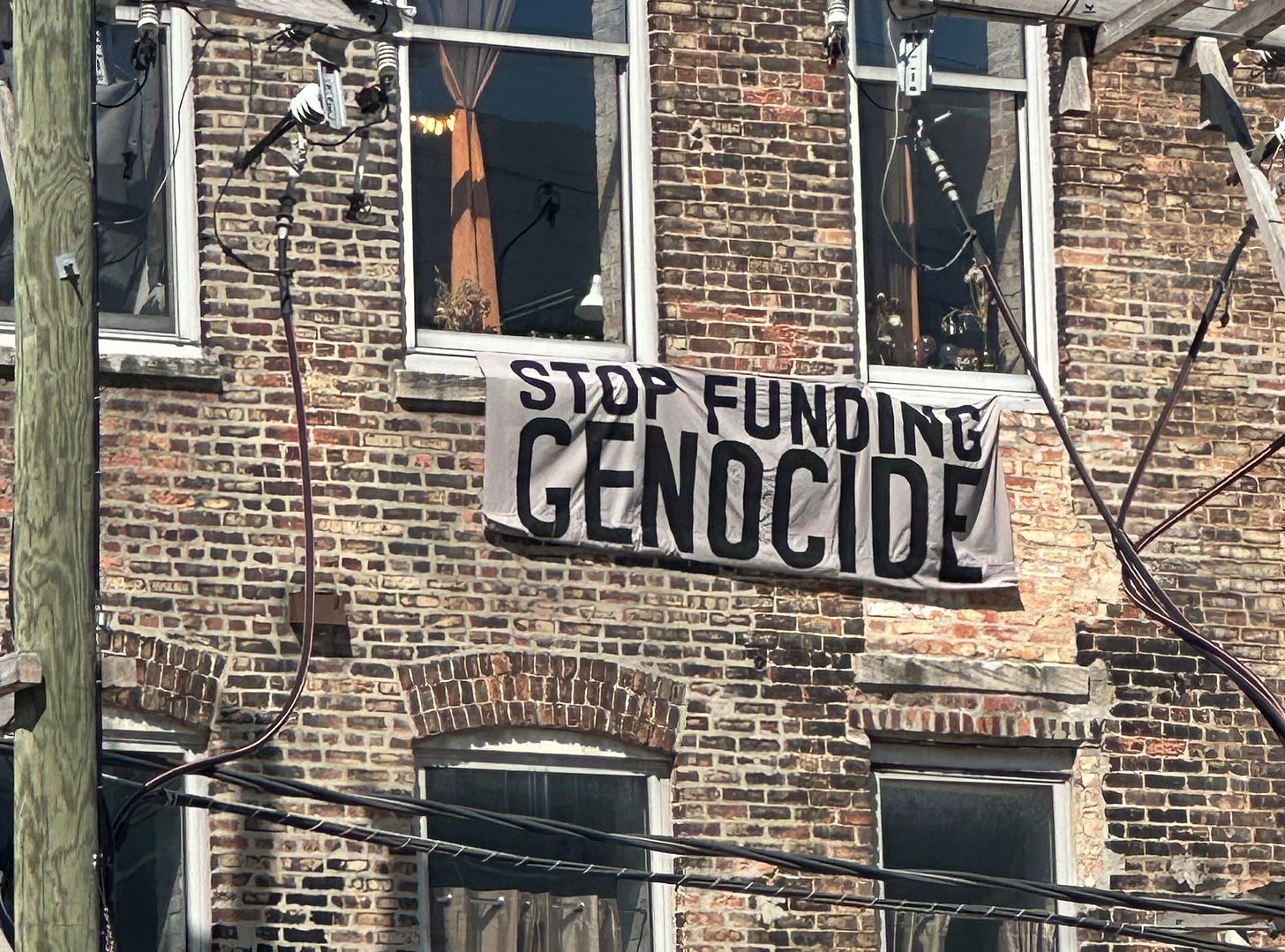 A banner saying "Stop Funding Genocide" hanging from an apartment window near the DNC A banner saying "Stop Funding Genocide" hanging from an apartment window near the DNC