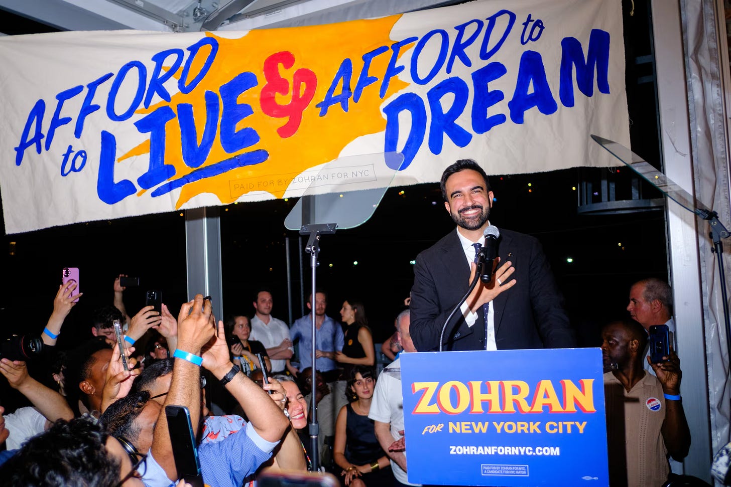Zohran Mamdani holds his hand over his heart behind a lectern that reads 'Zohran for New York City' at his election night party. Behind him a banner reads "Afford to Live & Afford to Dream" Zohran Mamdani holds his hand over his heart behind a lectern that reads 'Zohran for New York City' at his election night party. Behind him a banner reads "Afford to Live & Afford to Dream"