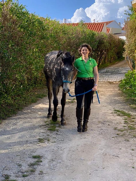 woman with small dark foal on lead, walking on cobbled lane